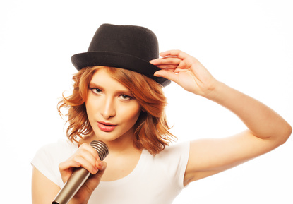 Happy singing girl. Beauty woman wearing white t-shirt and black hat with microphone over white background. Hipster style.